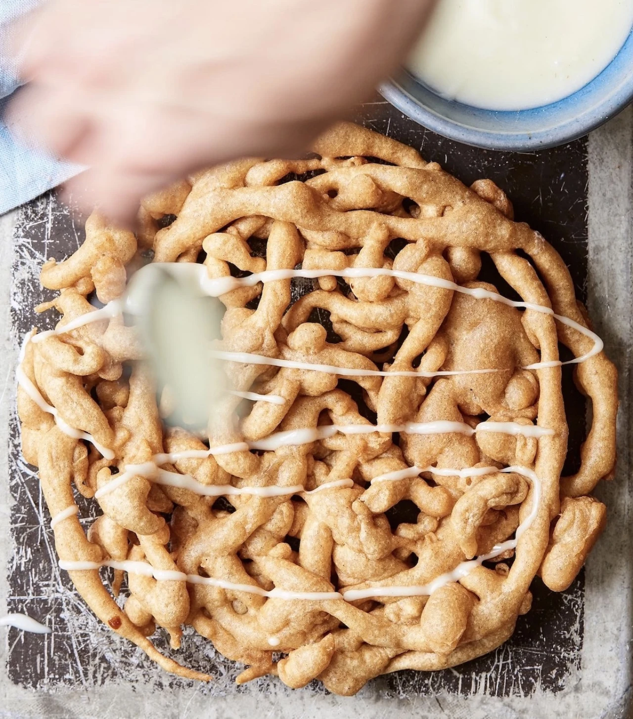 Freshly prepared funnel cake being finished with icing